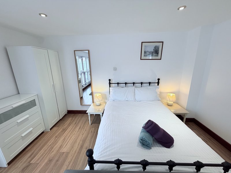 Bright bedroom with double bed, white wardrobe, mirror, bedside lamps and wooden flooring