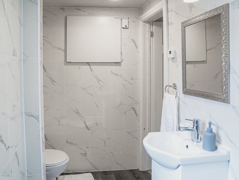 Modern bathroom with walk-in shower, white sink, toilet, and framed mirror
