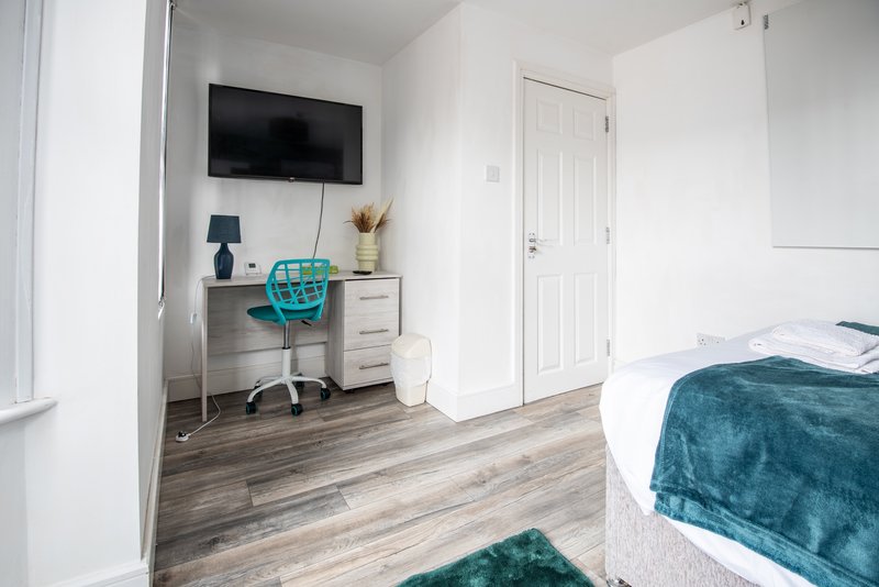 Bright bedroom with desk, wall-mounted TV, turquoise chair and beds