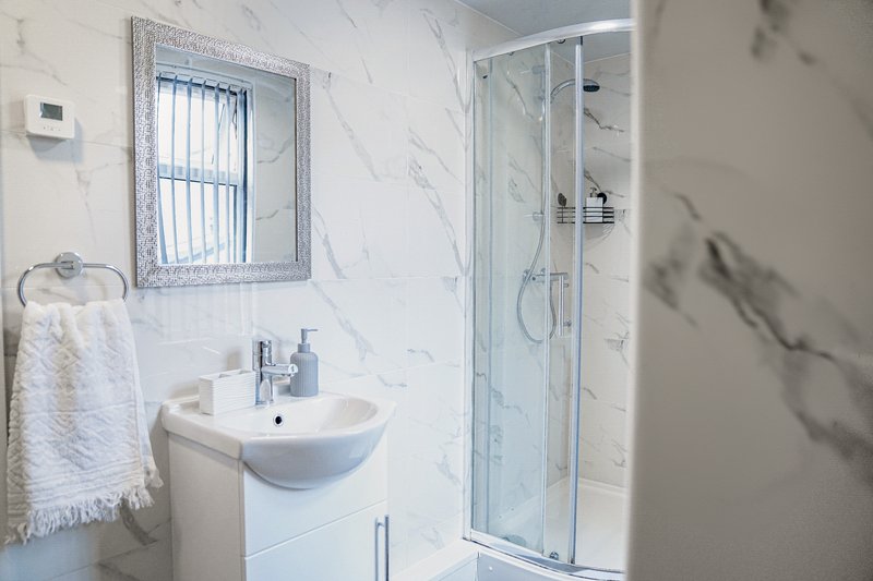 Modern bathroom with white sink, mirror, towel rail and glass shower enclosure