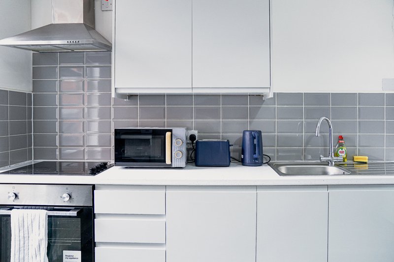 Modern kitchen with white cabinetry, gray tile backsplash, microwave, and countertop appliances