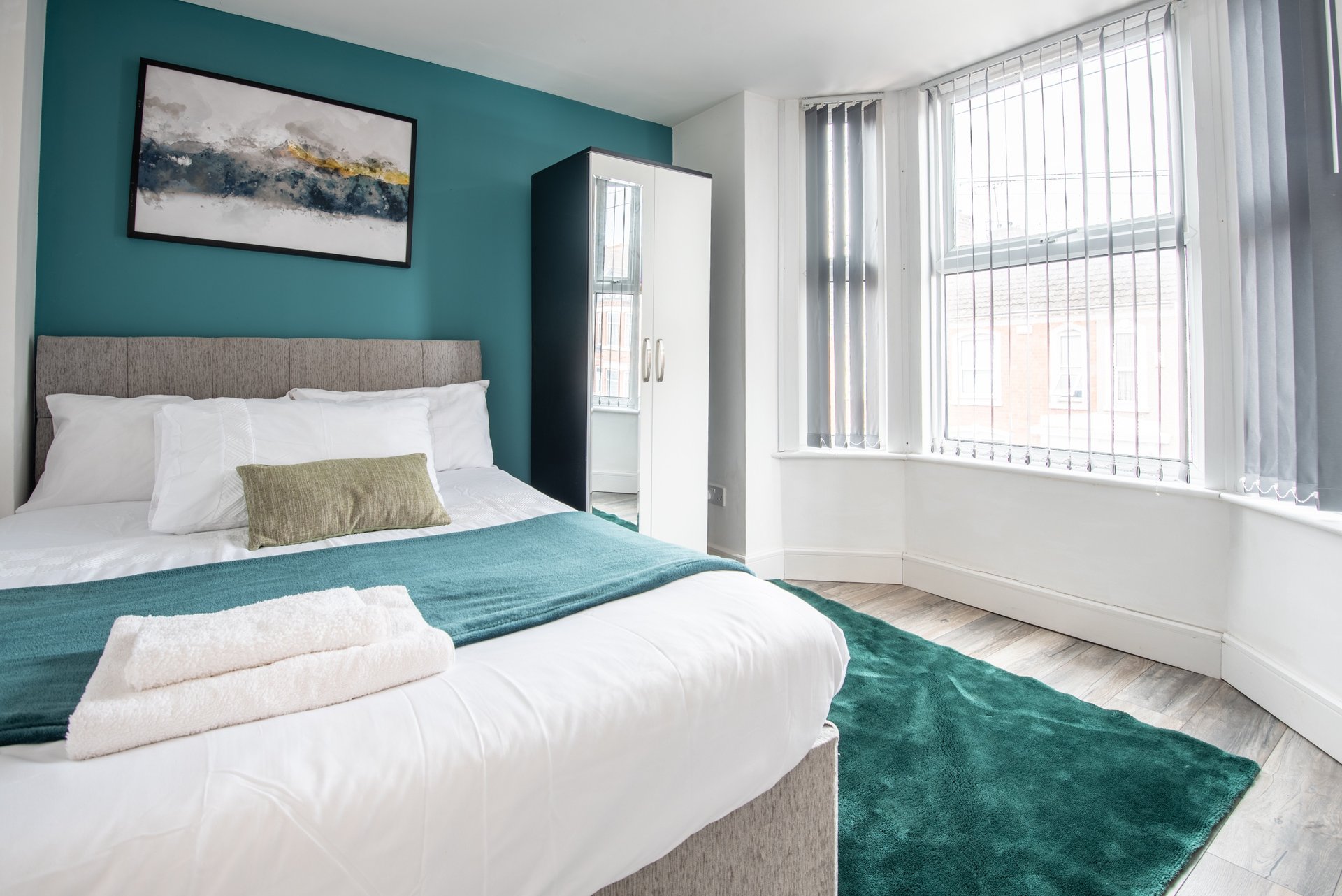 Modern bedroom with teal accent wall, two beds, white bedding, and large window