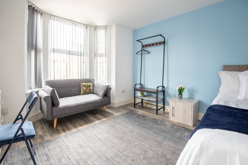 Bright bedroom with grey sofa, blue accent wall, wooden bed frame and large window