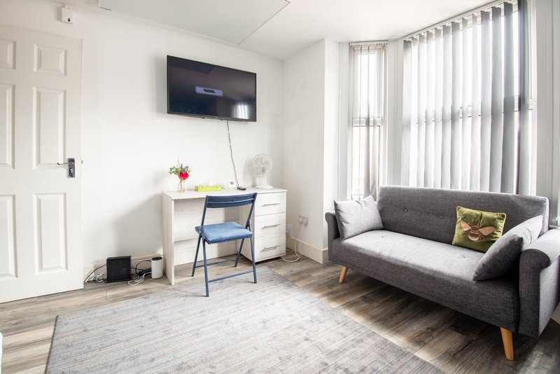 Studio living area with gray sofa, desk, chair, wall-mounted TV and bright windows