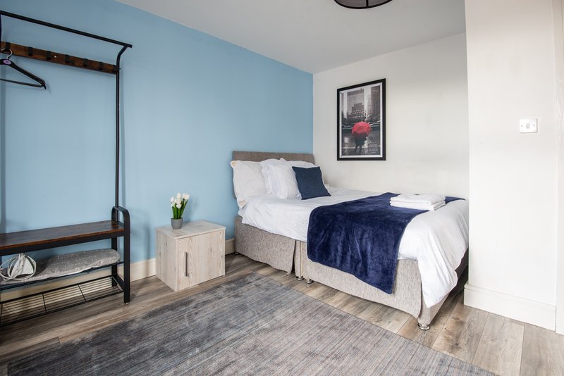 Bedroom with blue walls, double bed, wooden nightstand, framed artwork, and wooden flooring.