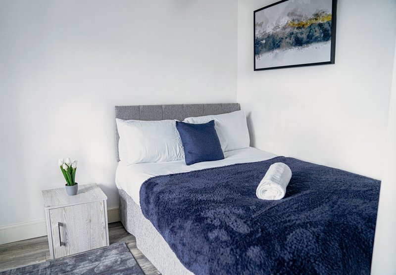 Modern bedroom with double bed, navy bedding, gray headboard, white nightstand with plant