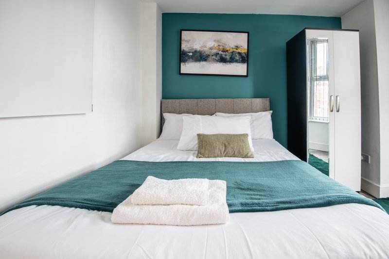 Bedroom with double bed, teal accent wall, framed artwork, and white wardrobe