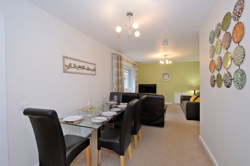Open-plan living and dining area with black dining table, chairs, sofa, and decorative plate wall display
