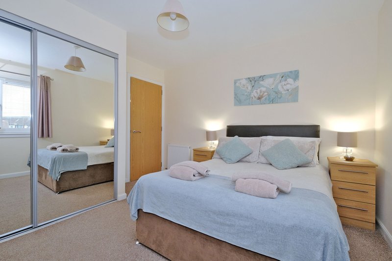 Modern bedroom with double bed, wooden nightstands, mirrored wardrobe and ensuite bathroom visible