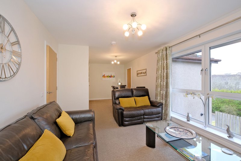 Open-plan living room with dark leather sofas, yellow cushions, large window and wall clock