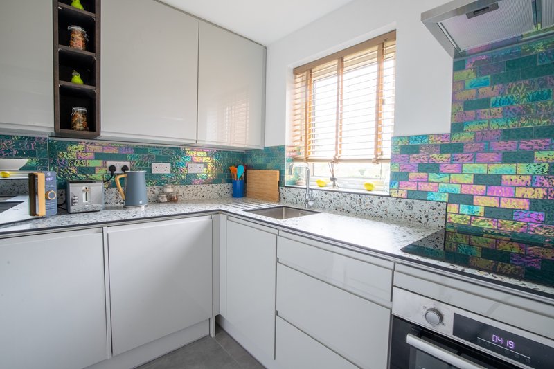 Modern kitchen with white cabinetry, colorful tiled backsplash, stainless steel appliances and window