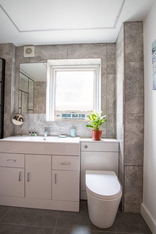 Modern bathroom with white vanity, toilet, mirror, window and gray tile walls