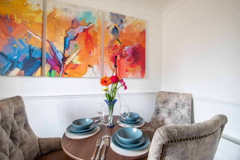 Dining room with round wooden table, four upholstered chairs, place settings, and colorful abstract wall art