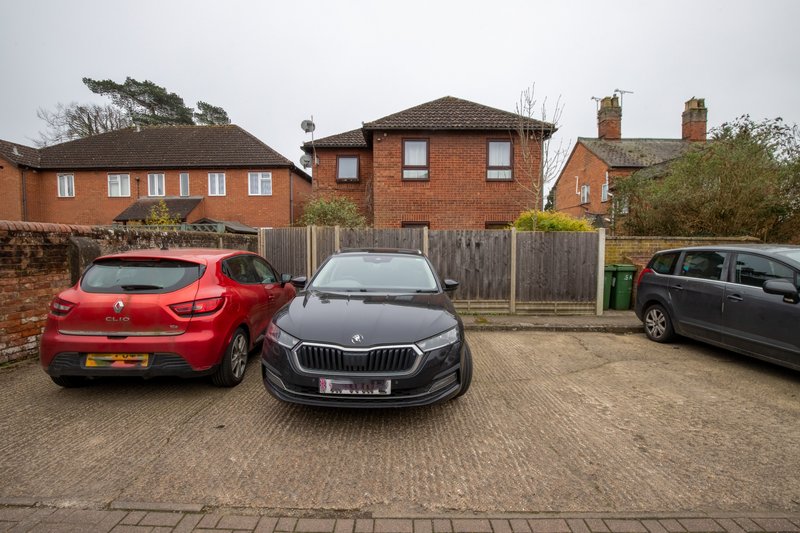 Brick property exterior with driveway, three parked cars, wooden fence and neighboring houses