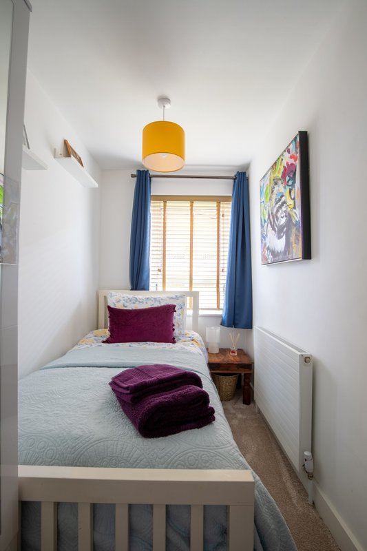 Compact bedroom with single bed, yellow pendant light, blue curtains and burgundy cushion