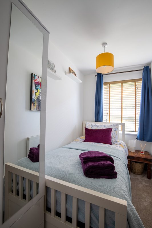 Small bedroom with single bed, yellow pendant light, blue curtains and mirrored wardrobe door
