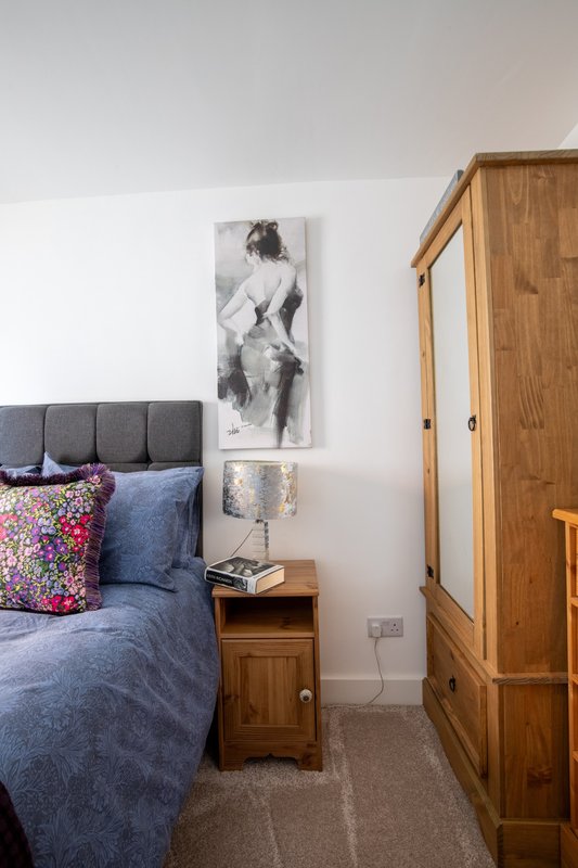 Bedroom with double bed, gray headboard, colorful cushion, wooden bedside table and wardrobe