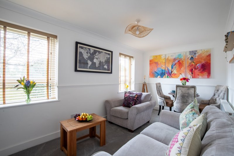 Bright living room with grey upholstered seating, wooden coffee table, framed artwork and colourful wall art