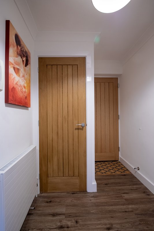 Hallway with wooden doors, white walls, wood flooring and ceiling light