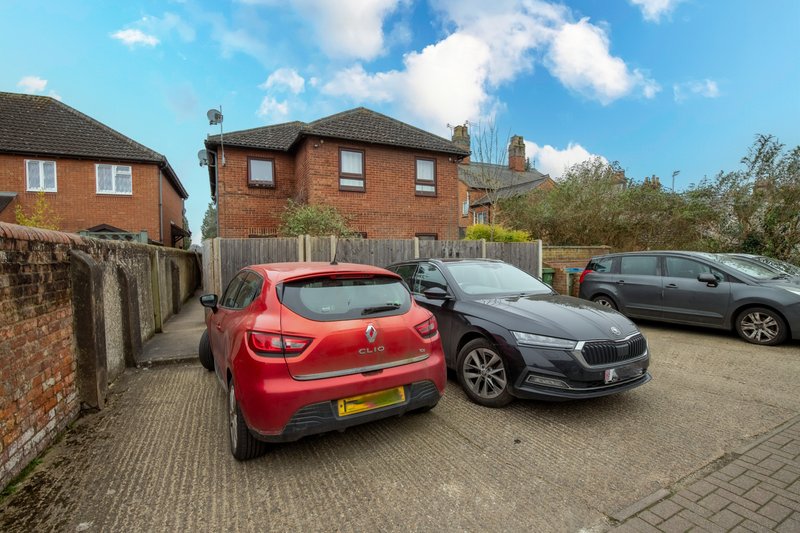 Brick residential property with driveway, parked cars, and neighboring houses visible