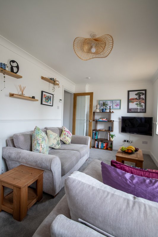 Bright living room with grey sofas, wooden coffee table, wall-mounted shelving and woven ceiling pendant light