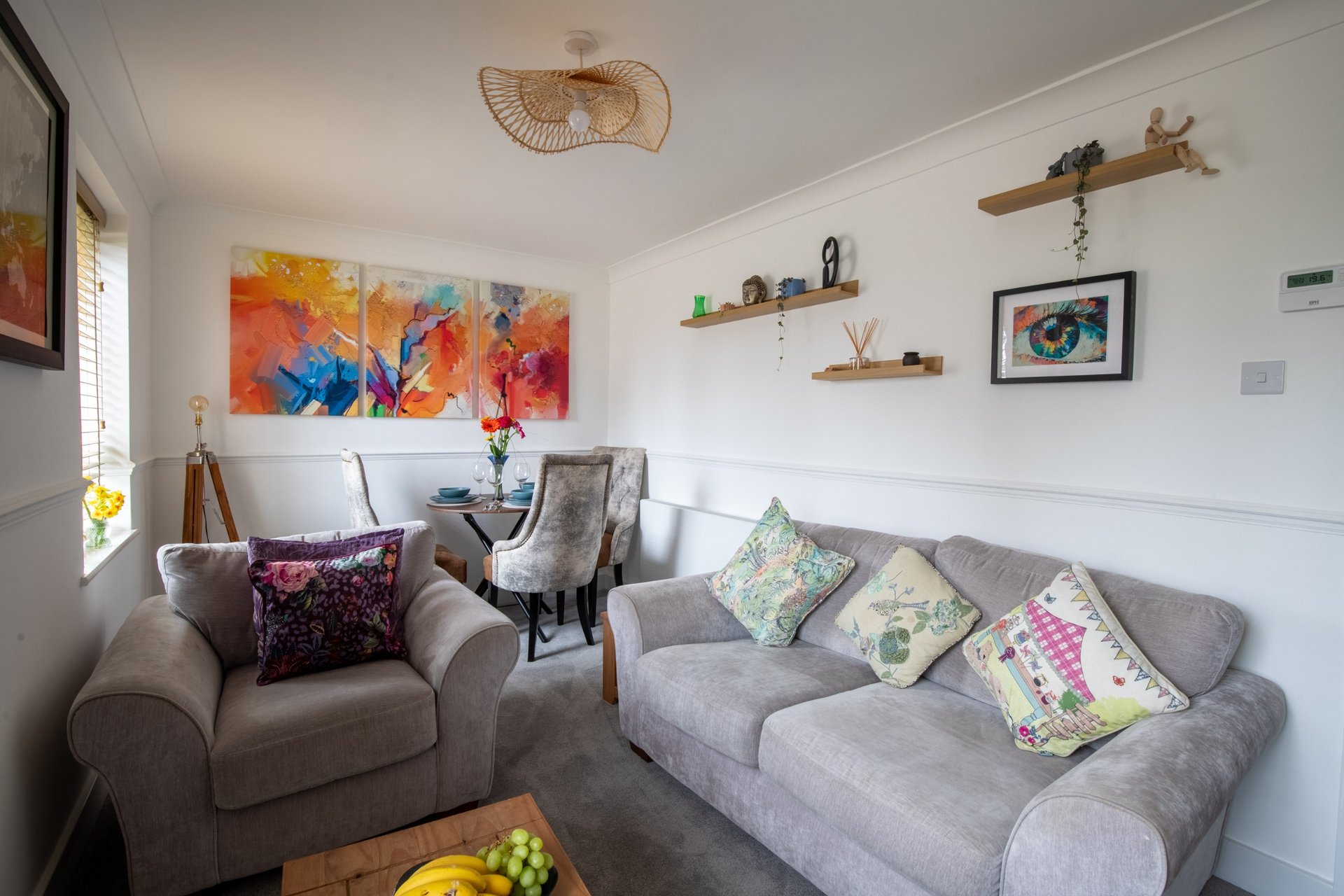 Bright living room with gray sofa, armchair, colorful abstract art, and decorative shelving
