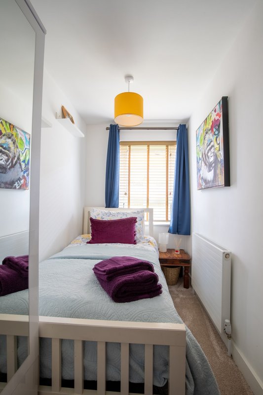 Compact bedroom with single bed, yellow pendant lamp, blue curtains and wall art