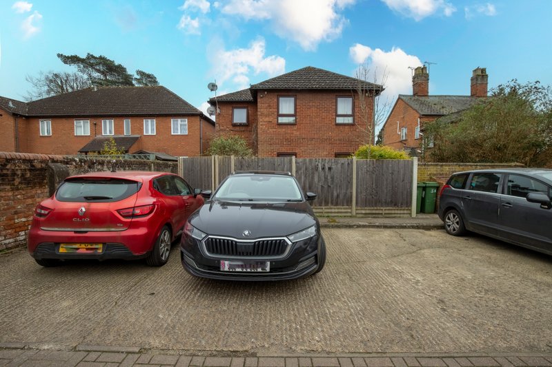 Brick detached house with driveway, three parked cars, wooden fence and garden