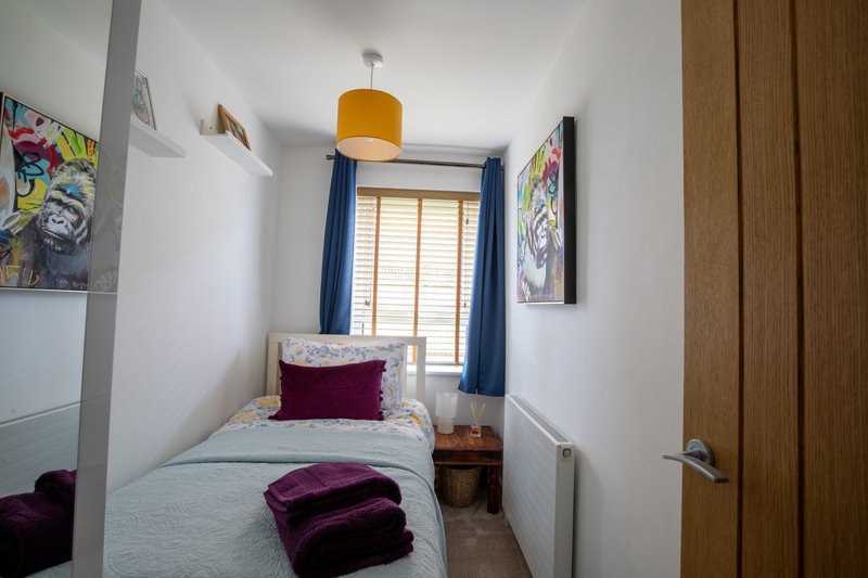 Compact bedroom with single bed, yellow pendant light, blue window shutters and wall art