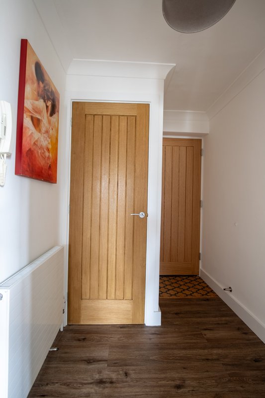 Hallway with wooden doors, white walls, dark wood flooring and abstract wall art