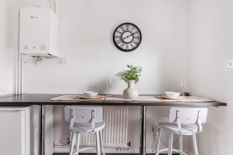 Modern kitchen counter with white chairs, potted plant, clock and wall-mounted boiler