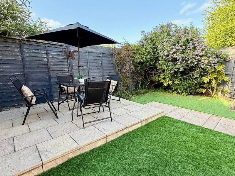 Garden patio with dining table, chairs, and canopy umbrella overlooking manicured lawn