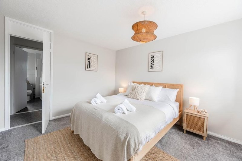 Bright bedroom with wooden bed frame, white bedding, natural light fixture, and ensuite door