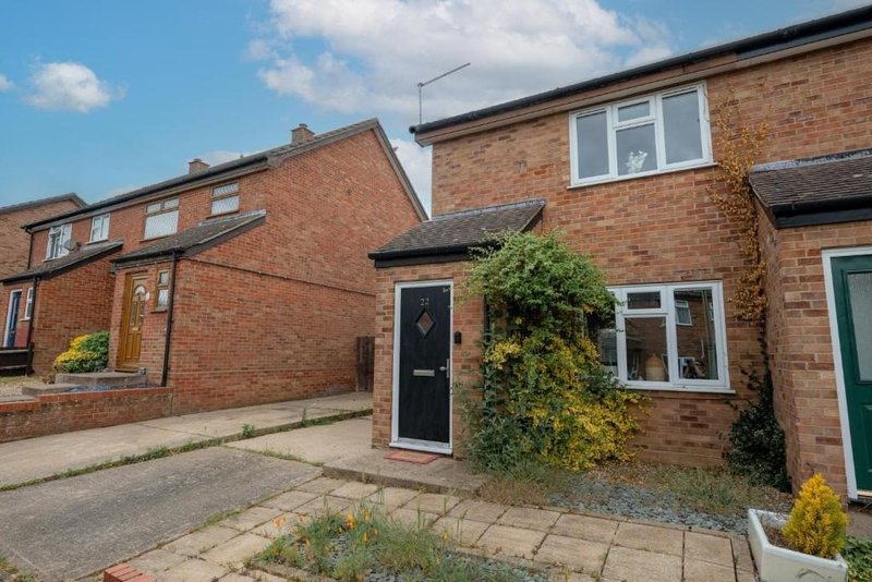 Brick semi-detached house exterior with black door, ivy-covered wall, driveway and front garden