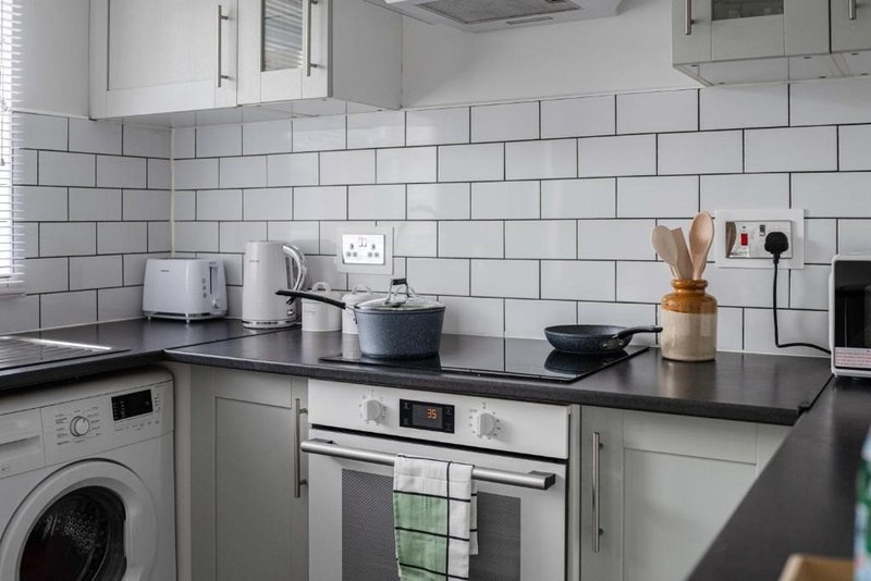 Modern kitchen with white subway tiles, black countertop, washing machine and integrated oven