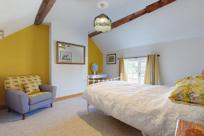 A bright and characterful double bedroom with exposed wooden beams, a comfortable bed and a cosy seating area. Beautiful countryside-style touches create a welcoming and relaxing space