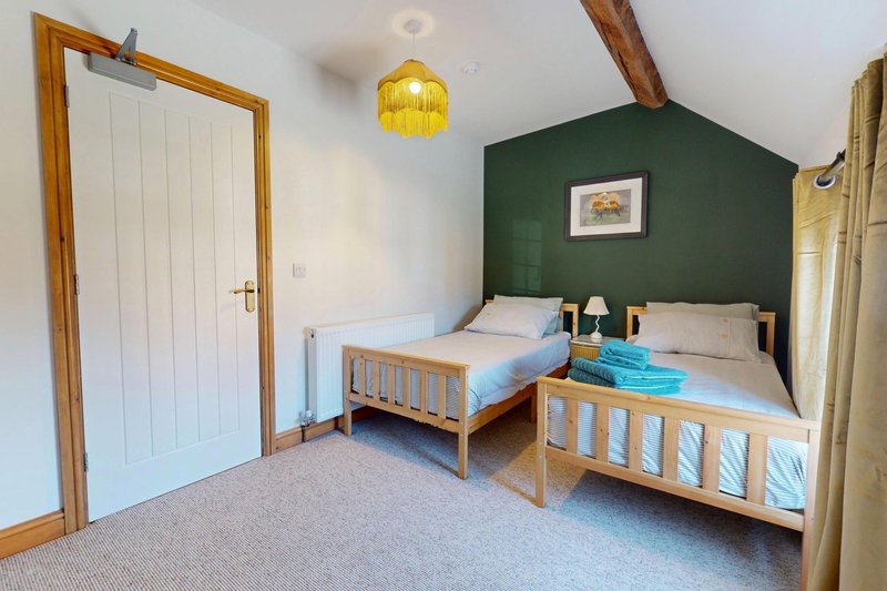 A spacious twin bedroom with two comfortable single beds, exposed wooden beams. Warm, homely touches and plenty of natural light create a relaxing space for guests.