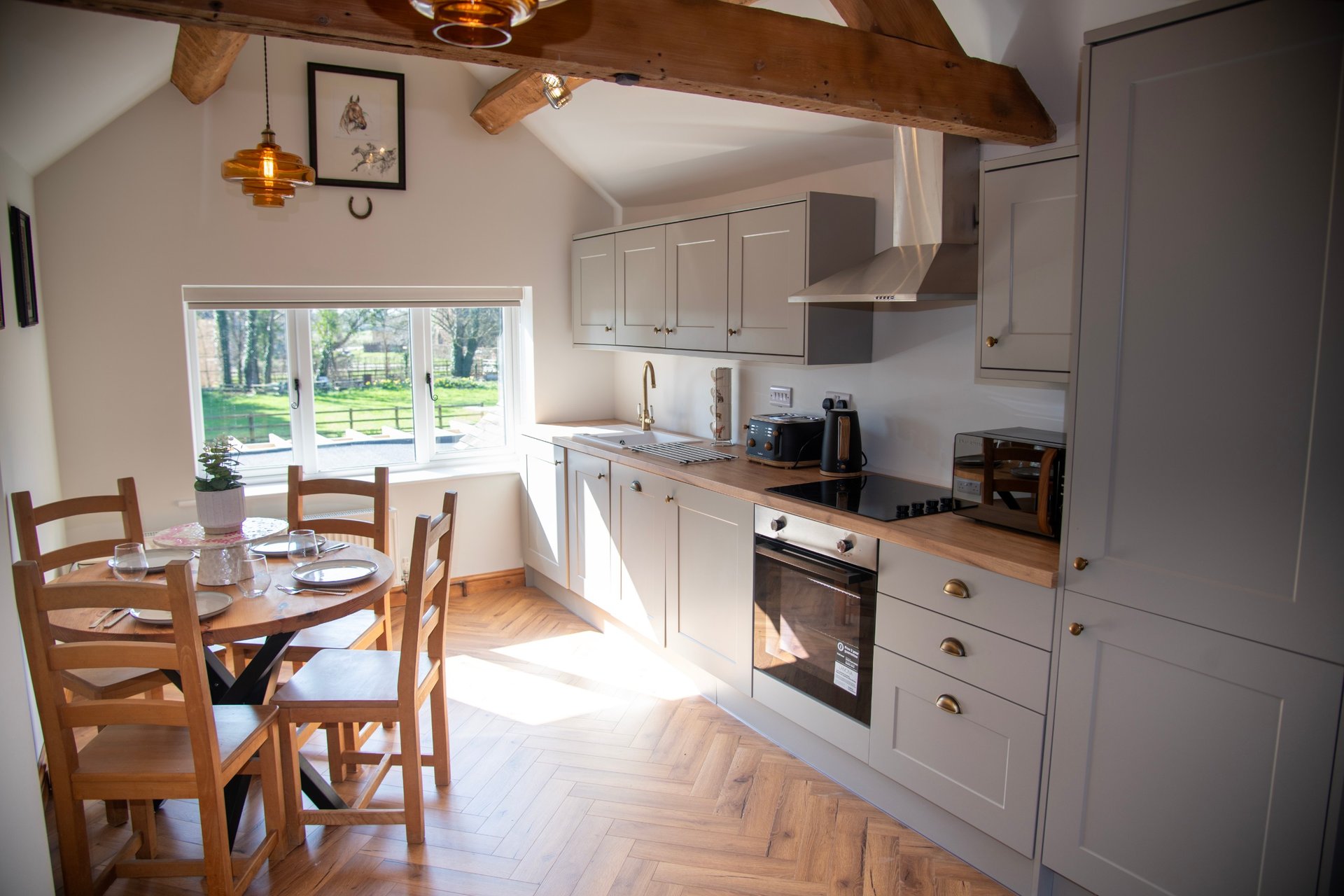 A bright, spacious and beautifully presented kitchen with a modern layout, exposed wooden beams and a charming dining area. The large windows fill the room with natural light offering lovely views