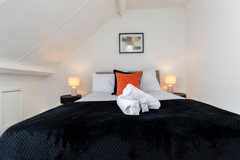Bright attic bedroom with double bed, black quilted duvet, orange cushion and white towels