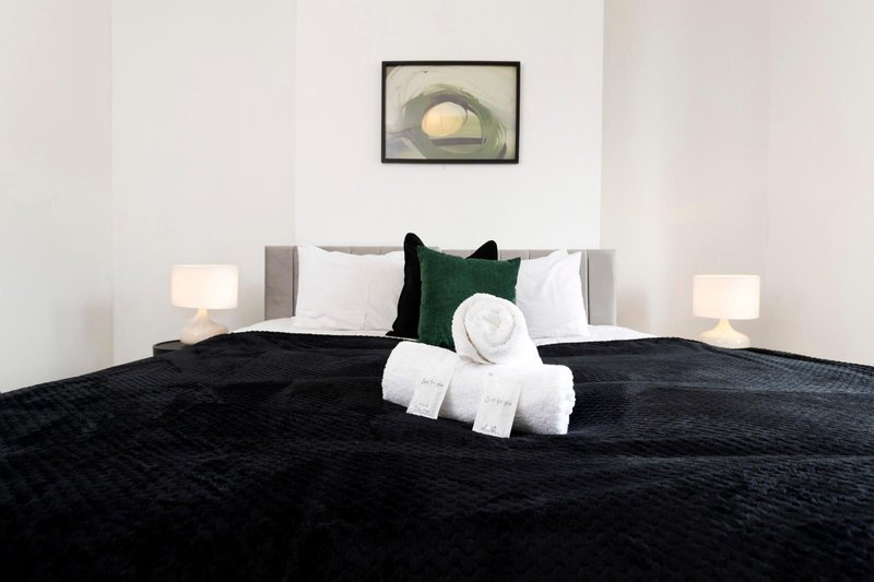 Modern bedroom with black duvet, grey headboard, white pillows, green cushion and bedside lamps
