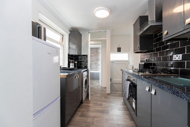 Modern galley kitchen with dark cabinets, white fridge, black subway tile backsplash and wooden flooring