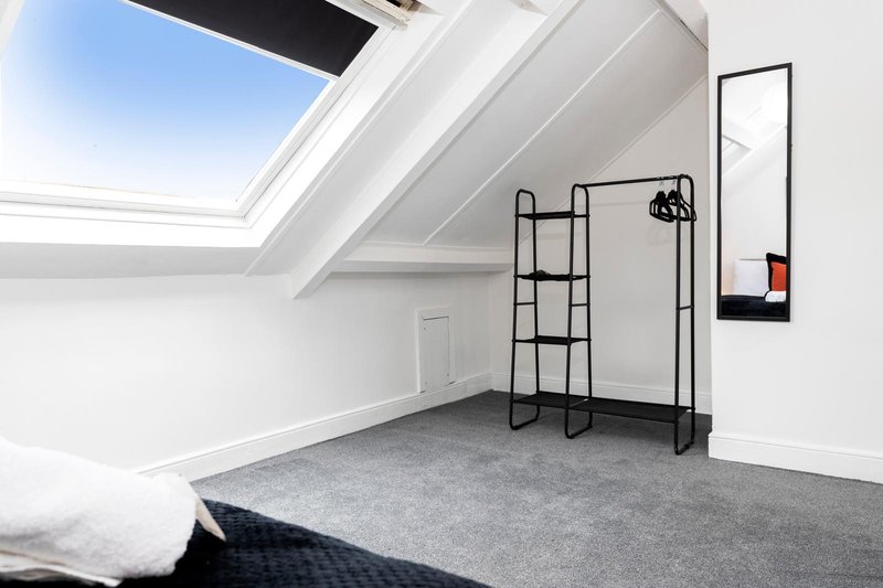 Bright attic bedroom with skylight, grey carpet, metal shelving and clothing rack