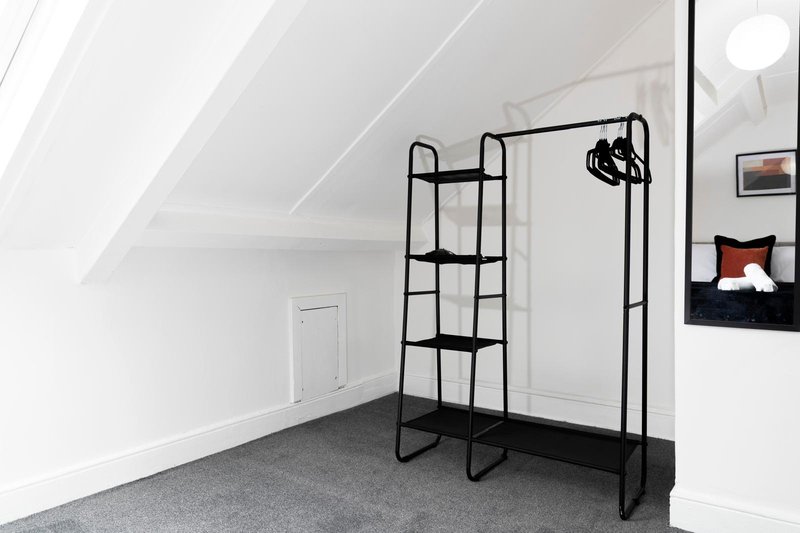 Minimalist attic bedroom with angled ceiling, black metal clothing rack and sloped white walls