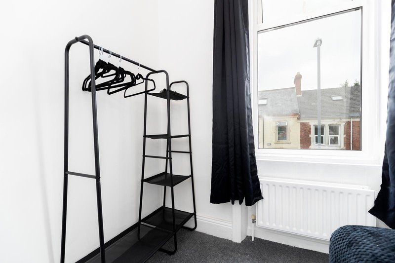 Bedroom corner with black clothing rack, window overlooking street, dark curtains and radiator