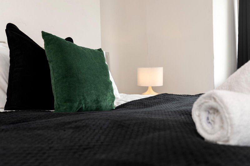 Bedroom bed with black and green decorative pillows, lamp and rolled towel