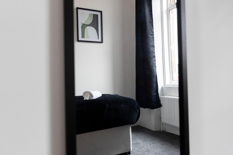 Bedroom with single bed, black bedding, framed wall art, window with radiator