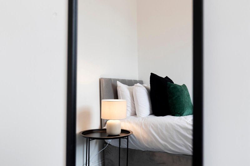 Bedroom view through doorway with bed, pillows, bedside lamp and small table