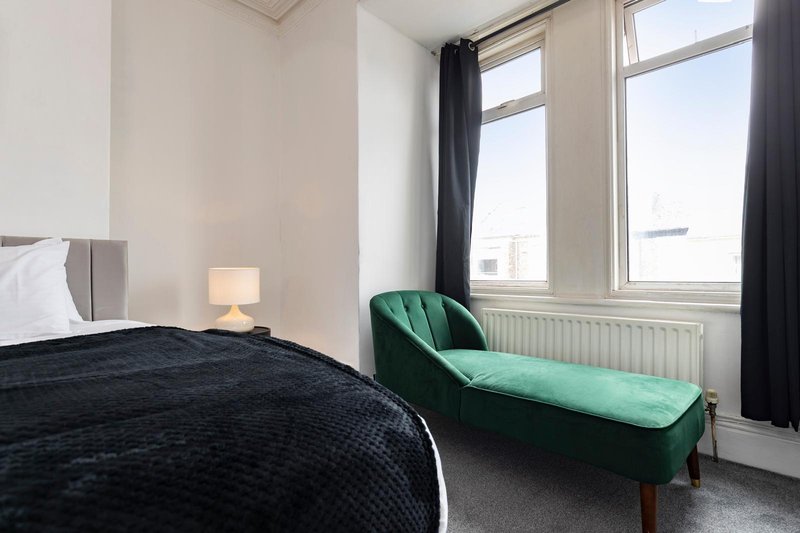 Modern bedroom with double bed, green upholstered bench, bedside lamp and large windows