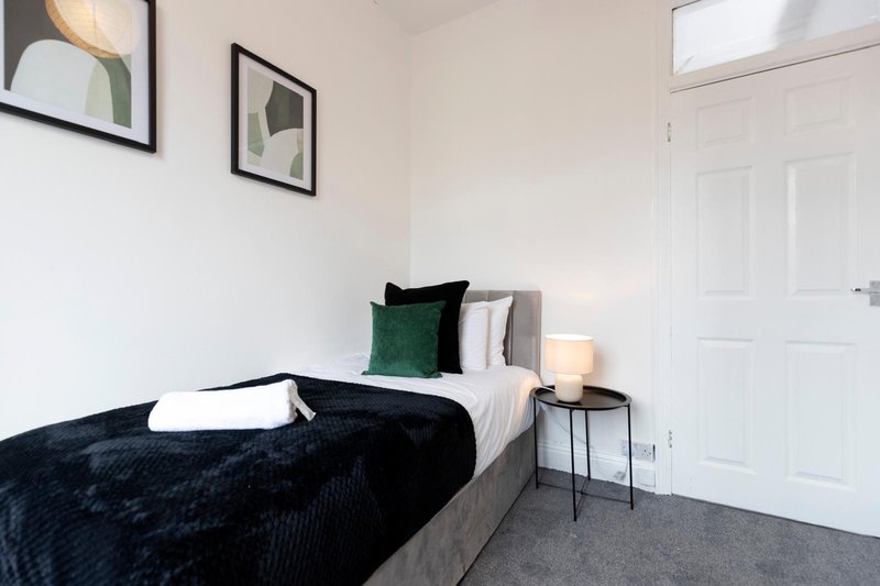 Bedroom with single bed, dark bedding, green and white pillows, side table with lamp