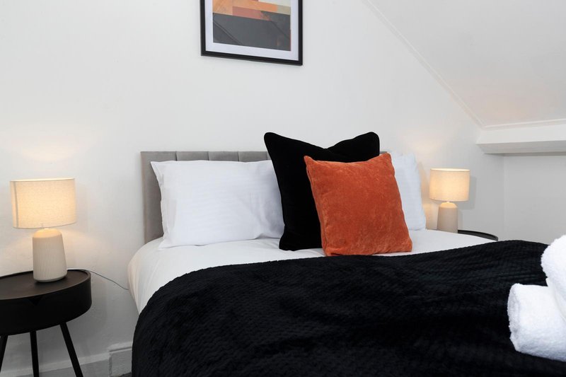 Modern bedroom with gray upholstered headboard, white pillows, black throw blanket, and orange accent cushion